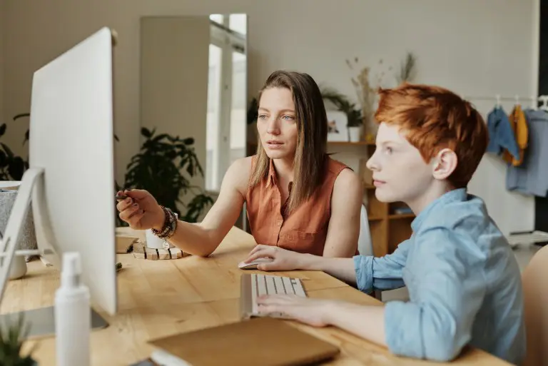 A woman and boy sitting at a table with a computer.