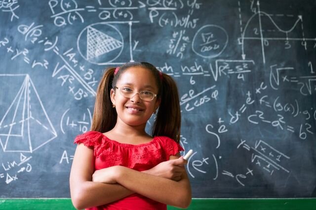 A girl in front of a chalkboard with equations on it.